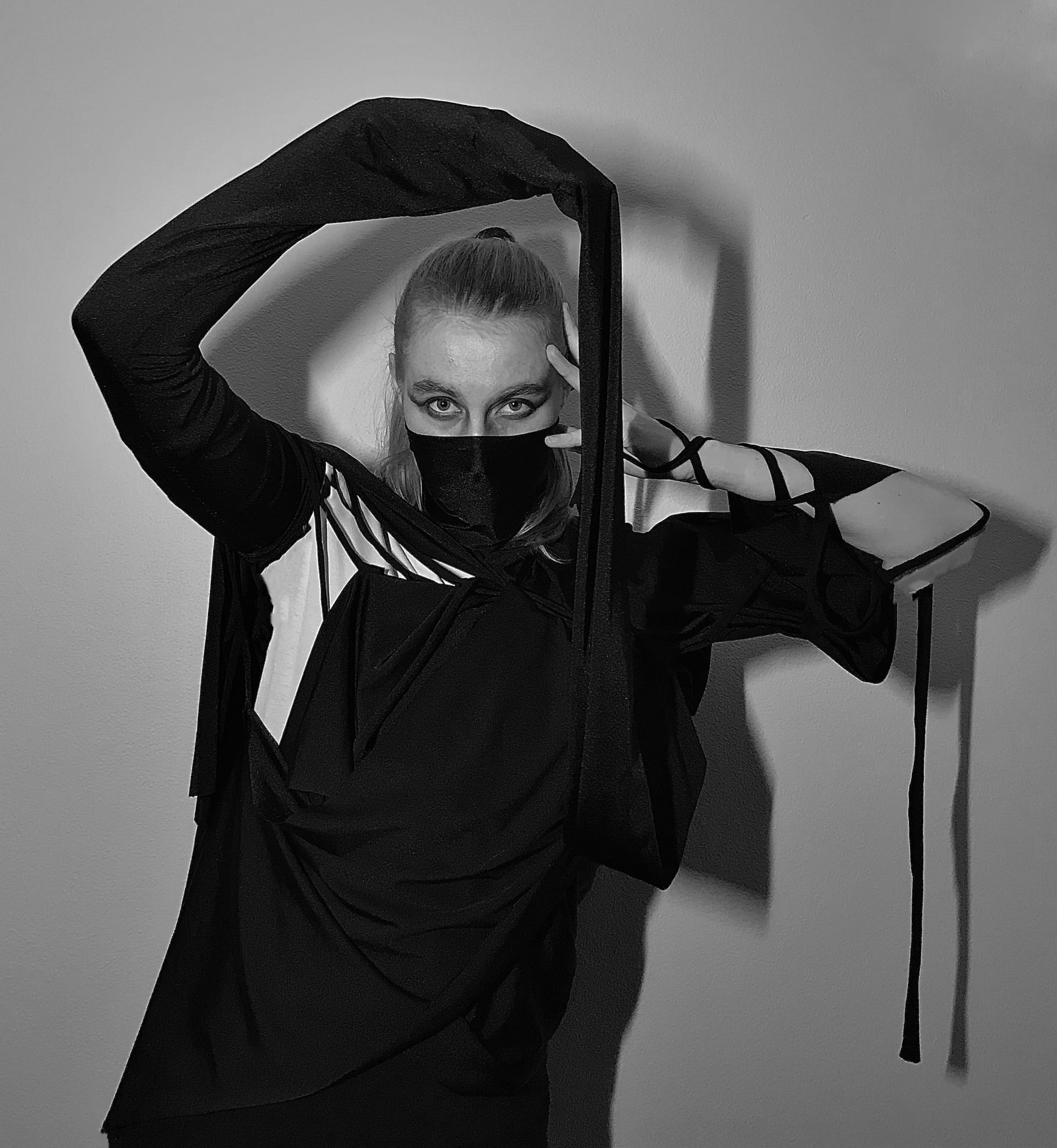 Model in a dark draped outfit with face covering, evoking confinement and anxiety